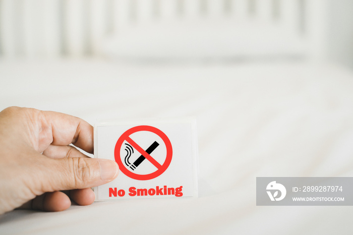 human’s hand holding no smoking sign with blurred bedroom , in soft focus