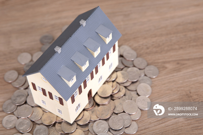 A small house model on a pile of dollar coins