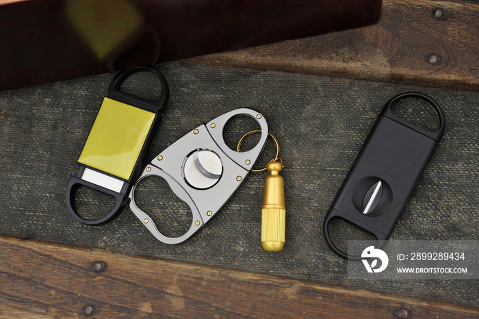 Flatlay Assortment of Cigar Cutters on Rustic Wood Table Beside Cigar Box