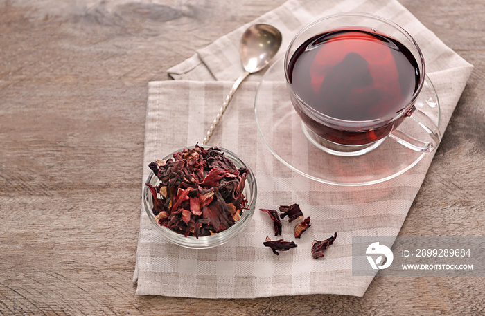 Bowl with dry hibiscus tea and cup of aromatic drink on wooden table