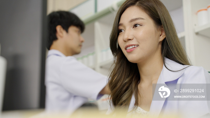 Happy Asian woman pharmacist in drugstore or pharmacy using computer