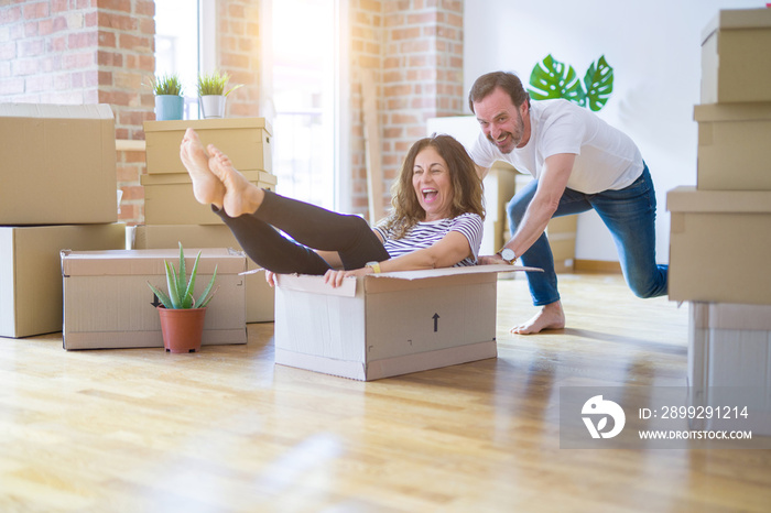 Middle age senior romantic couple having fun riding inside of cardboard, excited and smiling happy for moving to a new home