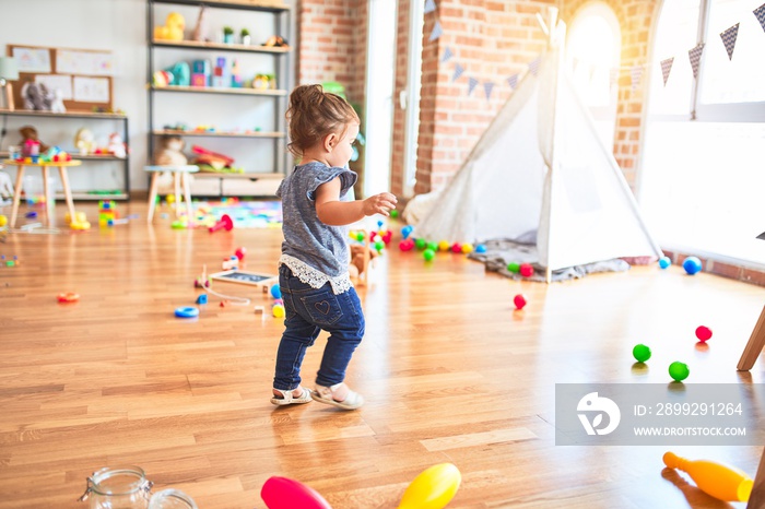 Beautiful toddler standing around lots of toys at kindergarten