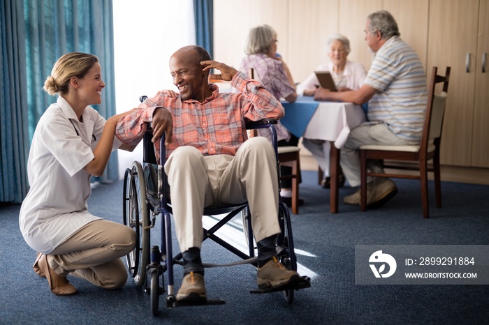 Smiling female doctor kneeling by disabled senior man sitting on