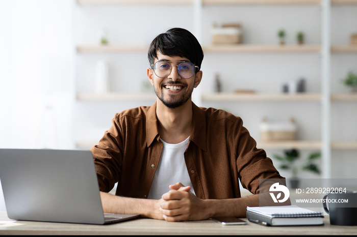 Cheerful indian entrepreneur working on laptop at office