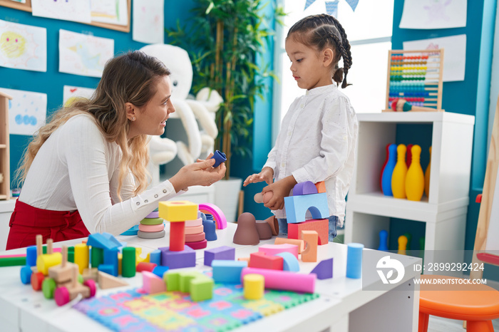 Teacher and toddler playing with geometry blocks sitting on table at kindergarten