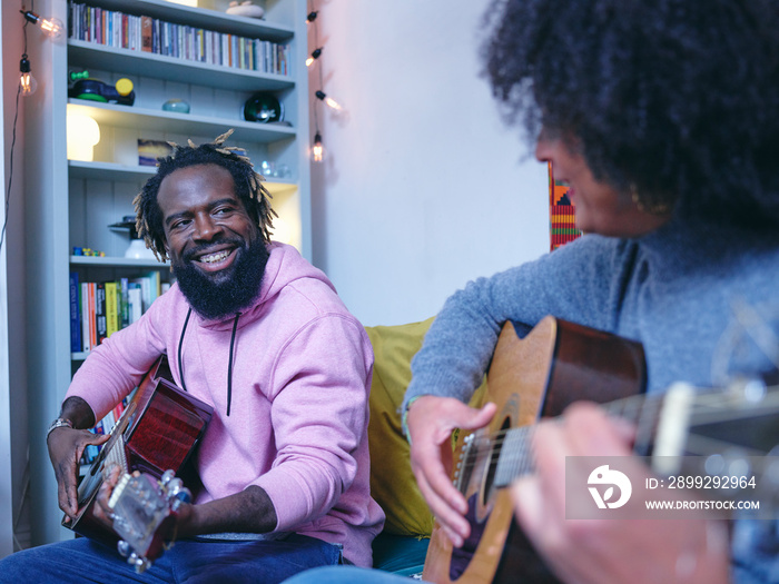 Couple playing acoustic guitars at home