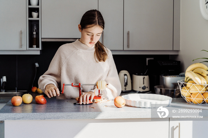 Teenager girl making making apple pie using apple peeler corer slicer machine. Child cooking at modern kitchen, preparing charlotte