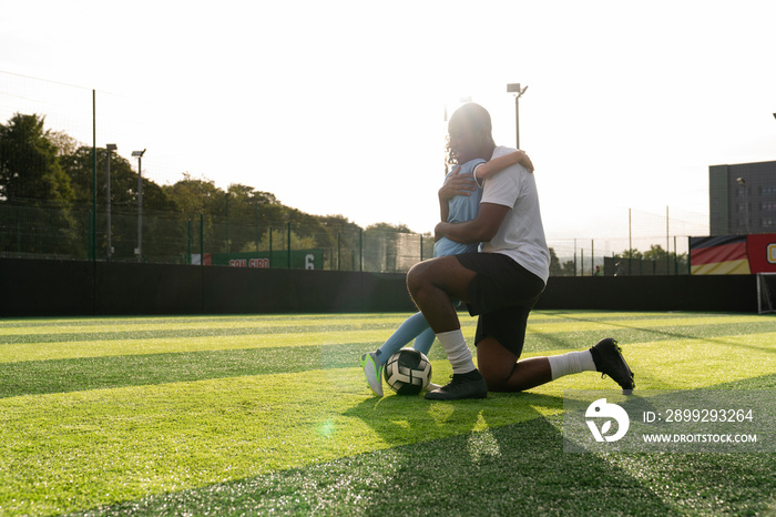 Coach and girl (6-7) hugging on soccer field