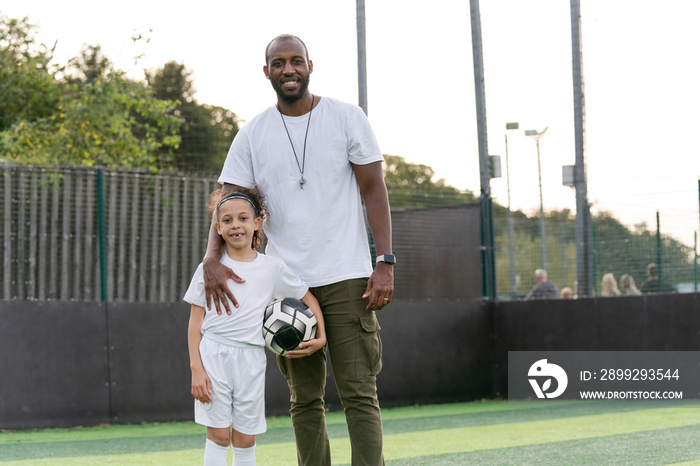 Portrait of man and girl (6-7) with ball on soccer field