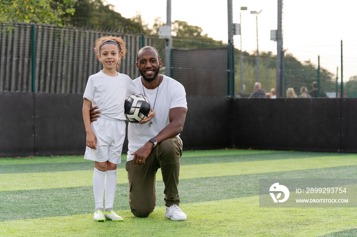 Portrait of man and girl (6-7) with ball on soccer field