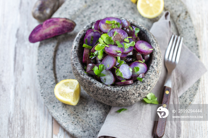 Chilean Chilotan Island cuisine. Purple violet potatoes salad with lemon, spring onion and cilantro in stone bowl. Gray Background