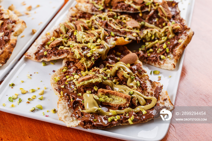 Bruschetta dolce fatta di pasta per la pizza con nutella, biscotti al pistacchio sbriciolati, crema di pistacchio e granella di pistacchio