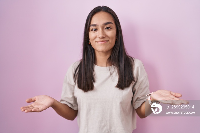 Young hispanic woman standing over pink background clueless and confused with open arms, no idea concept.