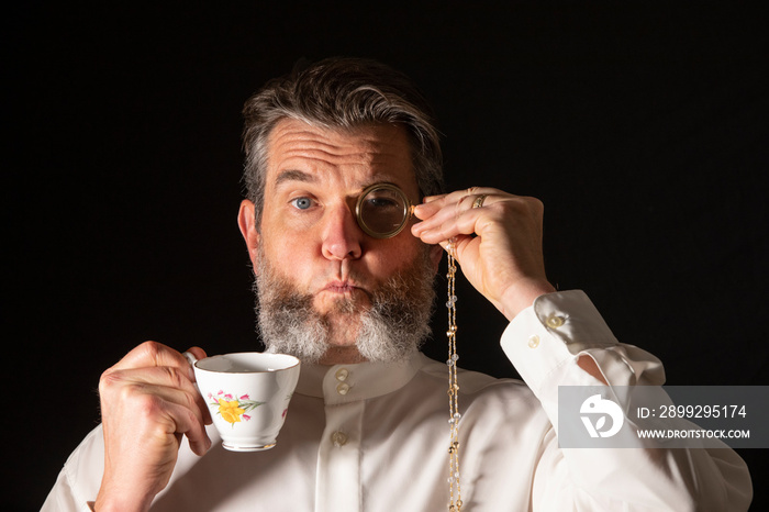 Man with muttonchops and funny expression holding monacle and cup of tea.