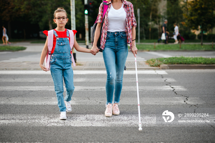 Young blind mother walking with her little daughter on city street.