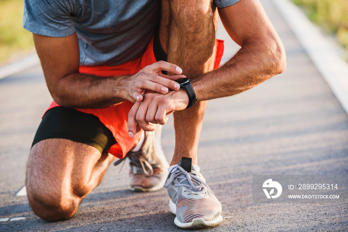 Young handsome sporty jogger taking break from exercising outdoors looking on a smart fitness watch