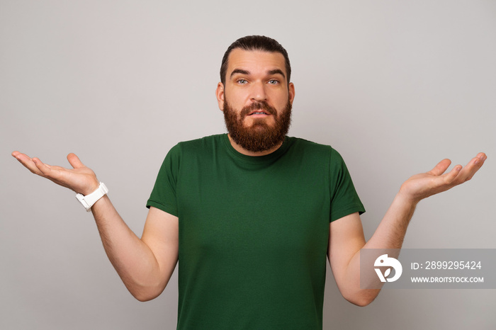 Confused young bearded man is shrugging his shoulder because he does not know what to answer.