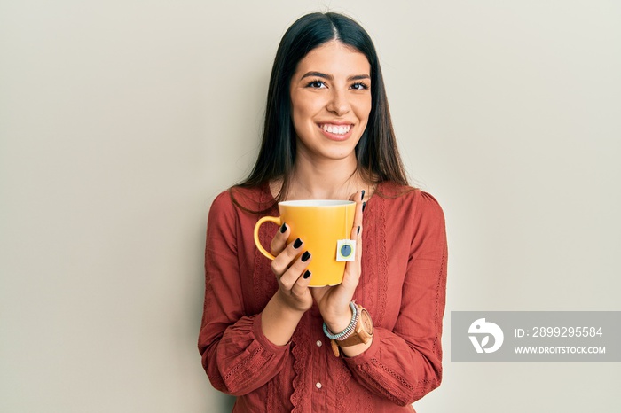 Young hispanic woman holding cup of tea smiling with a happy and cool smile on face. showing teeth.