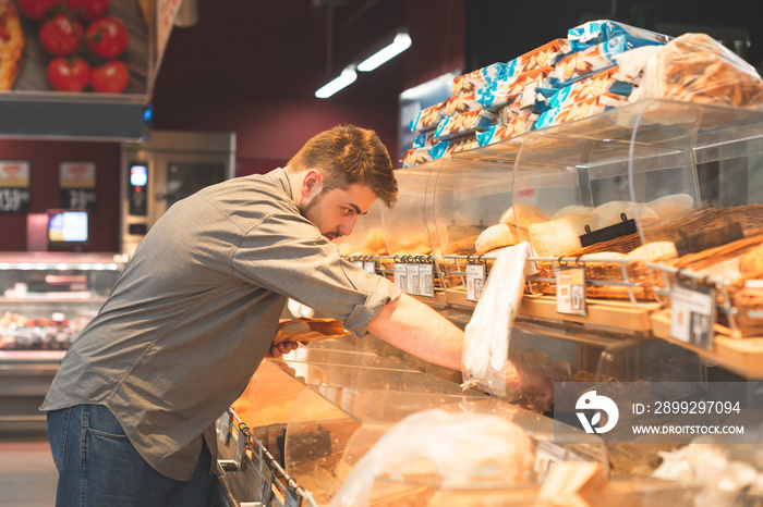 Adult takes fresh baked goods from supermarket shelves. Buyer buys buns in a supermarket. Hungry man chooses baked goods on the shelves of the store.