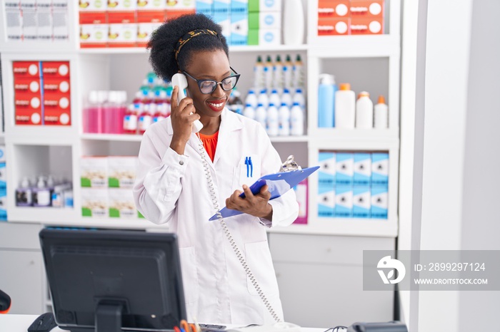 African american woman pharmacist talking on telephone reading document at pharmacy