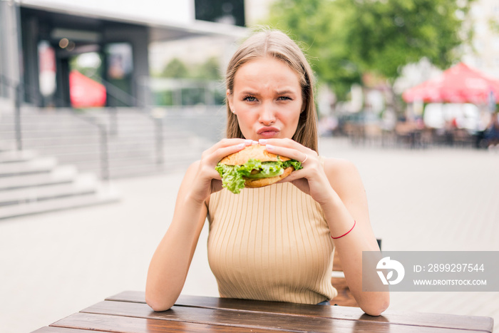 Young woman holding and eating eating tasty grilled burger outside in cafe