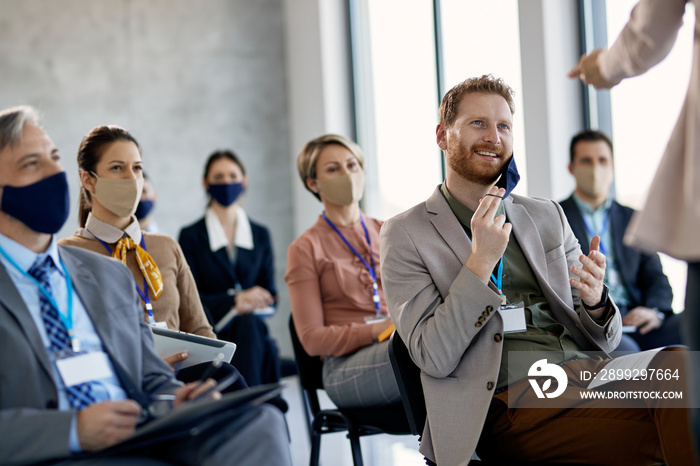 Happy businessman taking of protective face mask while talking to presenter during seminar.