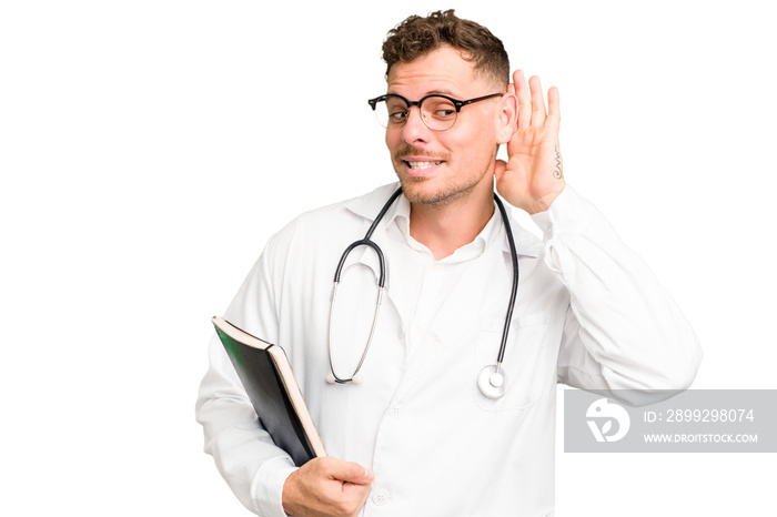 Young doctor caucasian man holding a book isolated trying to listening a gossip.