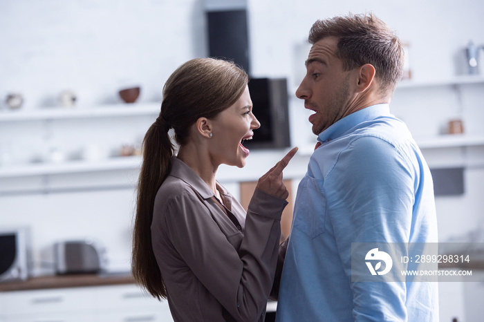 side view of angry woman pointing with finger and screaming at husband