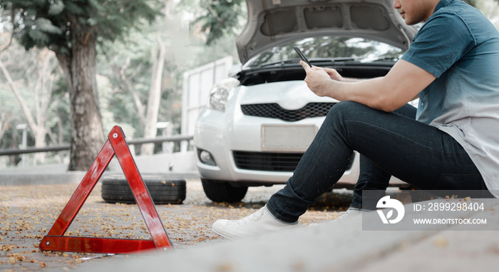 Asian man using smartphone for assistance after a car breakdown on street. Concept of vehicle engine problem or accident and emergency help from Professional mechanic