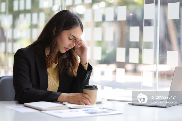 Tired businesswoman working in the office. Portrait of stressed lady with headache at desk. Tired overworked employee working with a laptop in an home office.