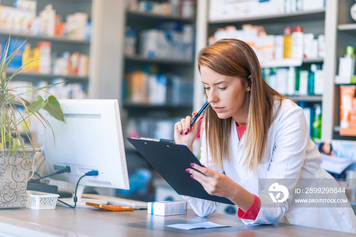 Pharmacist working in chemist shop or pharmacy. Junior pharmacist writing on clipboard at the hospital pharmacy. Busy Pharmacist Writing on Clipboard Taking a List of Medicine Pills in Pharmacy Shop