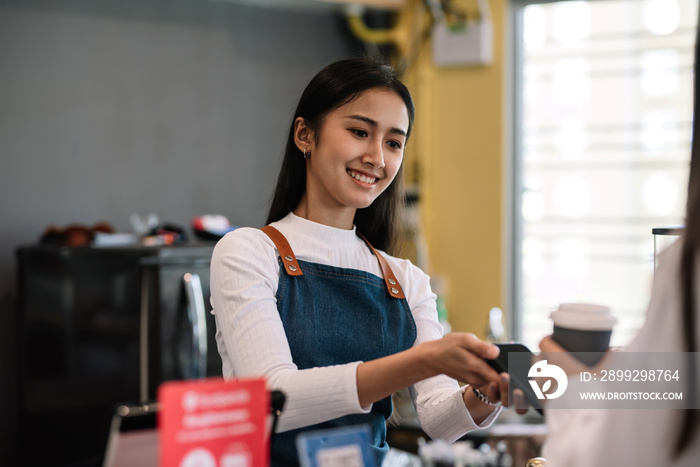 Young Asian woman café entrepreneur provides service by mobile payment at coffee shop.