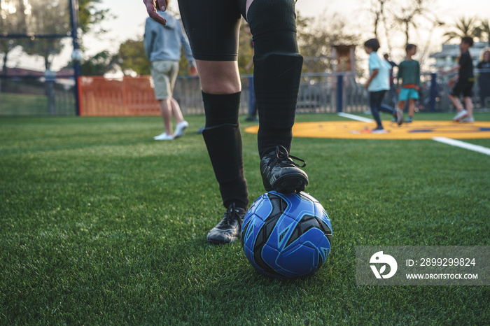 Crop anonymous soccer player with leg on ball standing on pitch