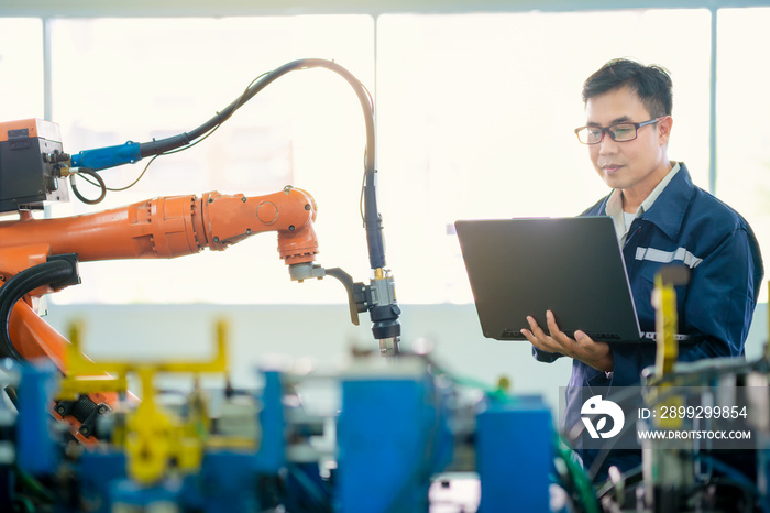 Automation concept: Asian senior robot training engineer is holding computer laptop ,check and monitoring  the data of welding robot in workshop.