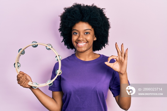 Young african american woman playing tambourine doing ok sign with fingers, smiling friendly gesturi