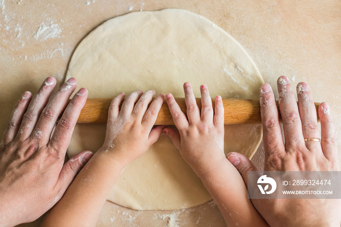 Child and dad hands rolling dough with rolling pin