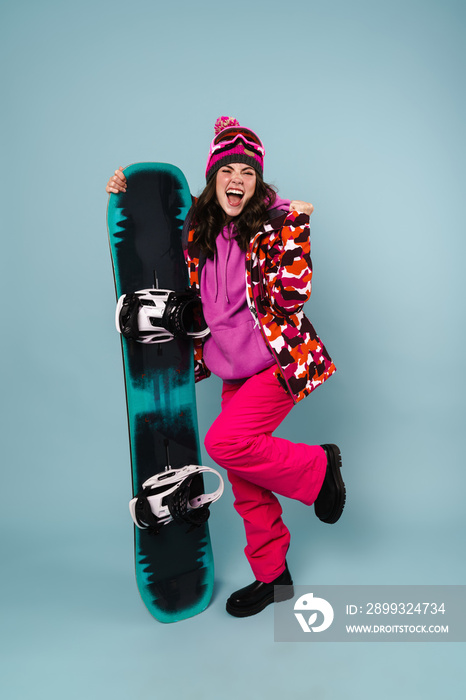 Excited sportswoman making winner gesture while posing with snowboard