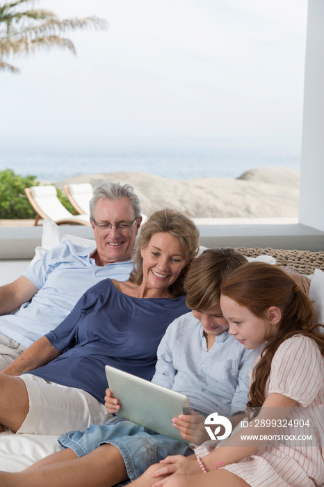 Grandparents and grandchildren using digital tablet on patio