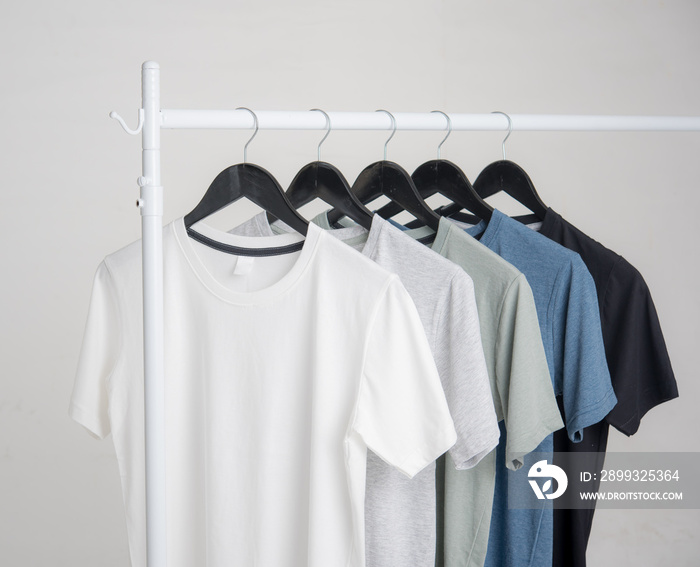 Black,blue, grey and white t-shirts on hangers on gray background