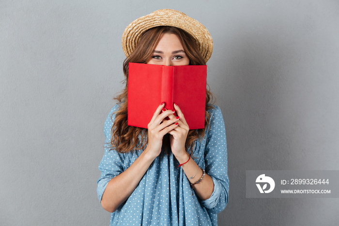 Woman standing over grey wall wearing hat covering face