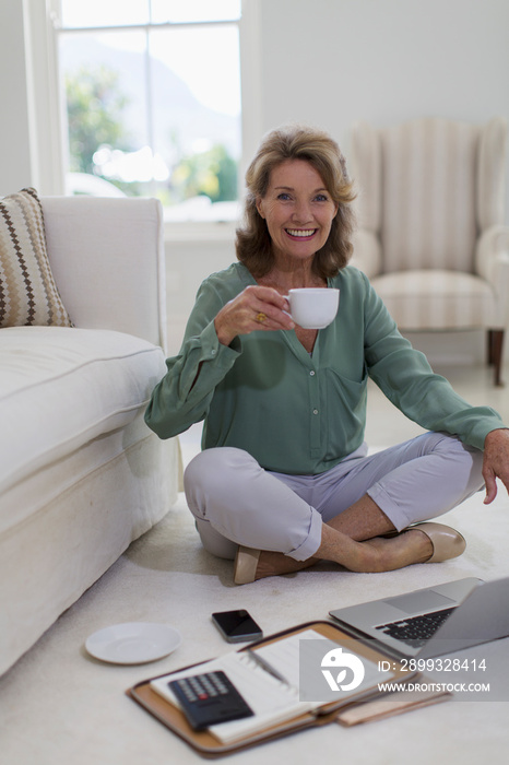 Portrait happy senior woman drinking coffee at laptop on floor