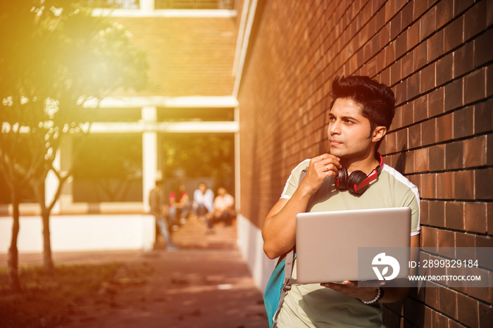 One Indian college student with laptop or book in focus with friends in the background out of focus