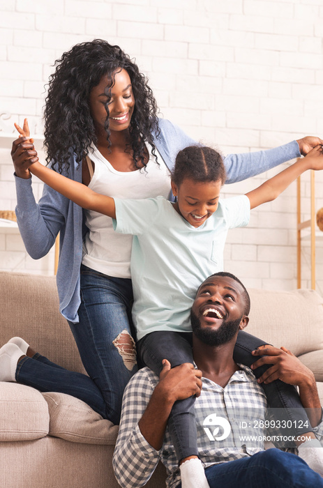 Joyful afro parents and their little daughter having fun at home