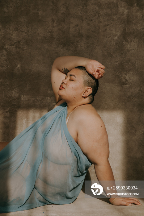 portrait of a plus size filipino woman with a shaved head basking in the sun eyes closed