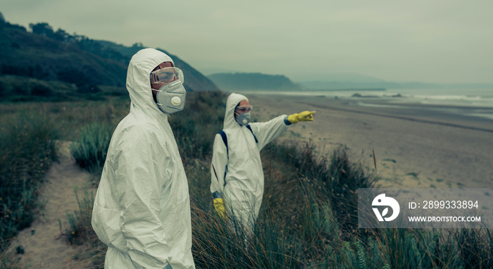 Man and woman in bacteriological protective suits watching and pointing to the sea