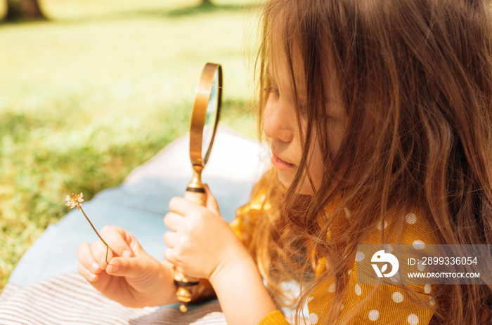 Closeup image of cute little girl exploring the nature with magnifying glass outdoors. Child playing