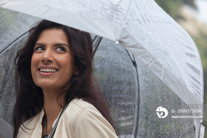 Smiling young woman with umbrella in rain