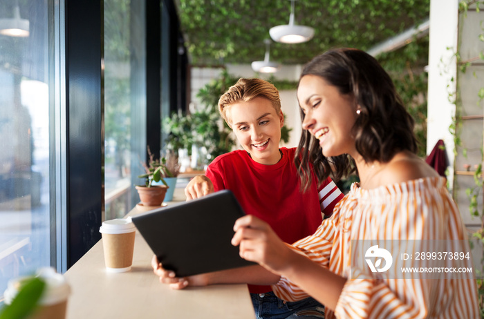 technology and people concept - female friends with tablet pc computer and coffee at cafe