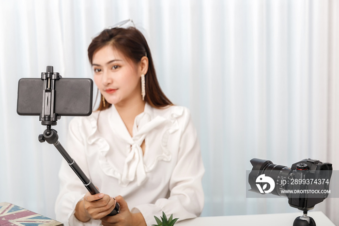 Young asian woman blogger selfie herself with smart phone while recording vlog video live streaming.